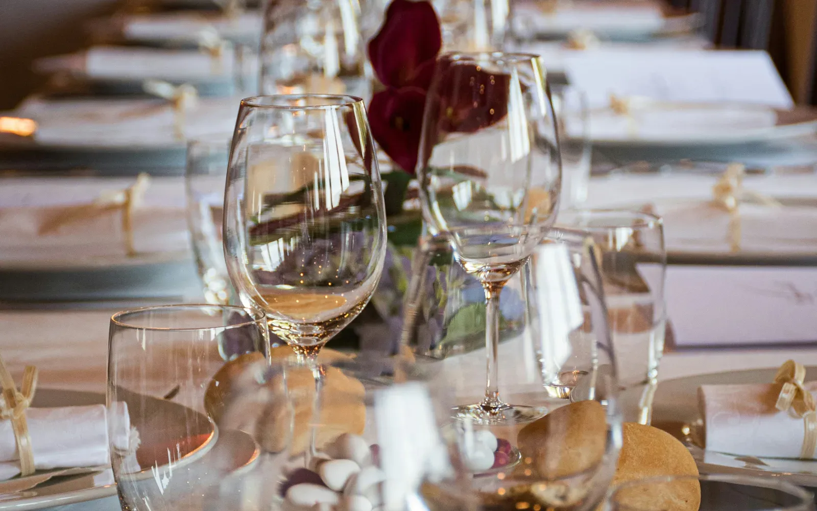 An elegantly set table with wine glasses, bread, and a single red rose